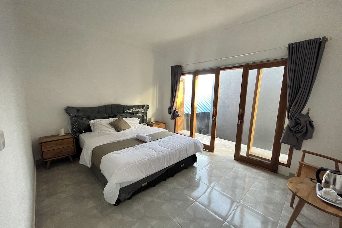 A bedroom with a bed, nightstands, a chair, and a view through a sliding glass door.