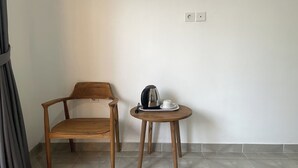 A wooden chair and a small round table with a kettle and cup, against a plain wall with a tiled floor. - Zee House (Canggu)