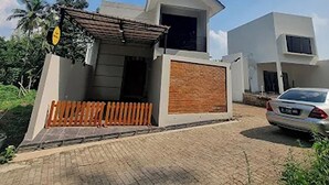 Una casa moderna de dos pisos con un porche cubierto, un camino de entrada cercado y un coche estacionado.