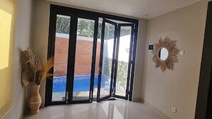 Una habitación con un amplio ventanal corredera que da a un espacio al aire libre, un espejo redondo en la pared y una planta en maceta.