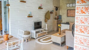 Una sala de estar moderna con pared de ladrillo blanco, muebles de madera, televisor de pantalla plana y objetos decorativos.