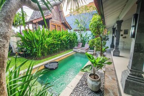 A pool area with a clear view of the surrounding garden, a seating area, and a traditional building in the background. - Villa Aris 1 Bali (Munggu)