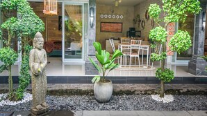 Una estatua de una figura en un jardín, con una mesa y sillas al fondo, que sugiere un espacio para comer o relajarse.