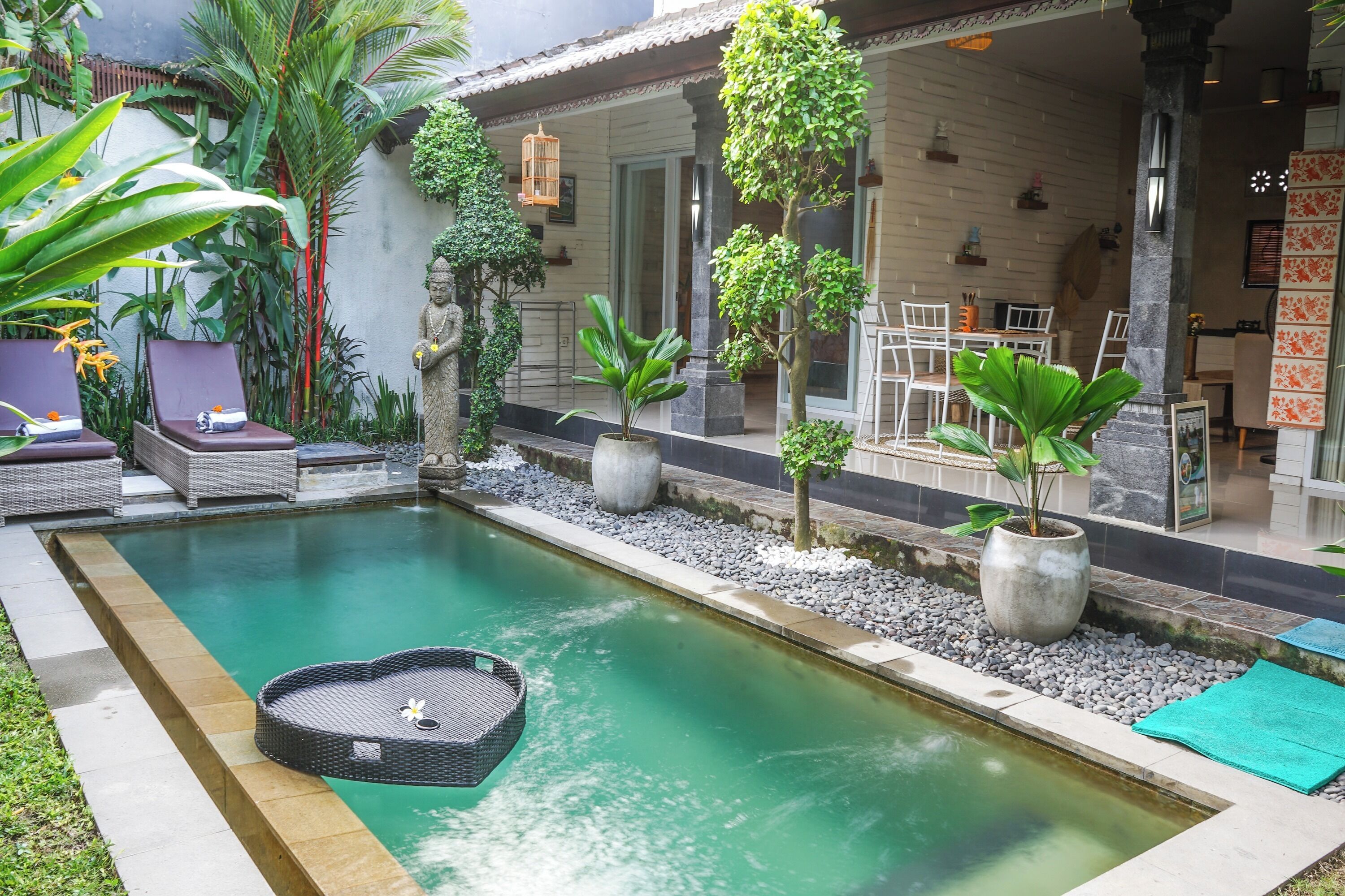 Ein Swimmingpool mit einer herzförmigen Schwimmplattform, umgeben von Topfpflanzen und einer Terrasse mit Gartenmöbeln.