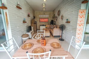 A dining area with a wooden table, white chairs, and woven placemats. - Villa Aris 1 Bali (Munggu)