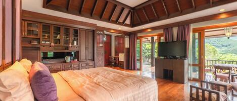A spacious bedroom with a large bed, wooden ceiling beams, a TV, and a balcony with a scenic view.