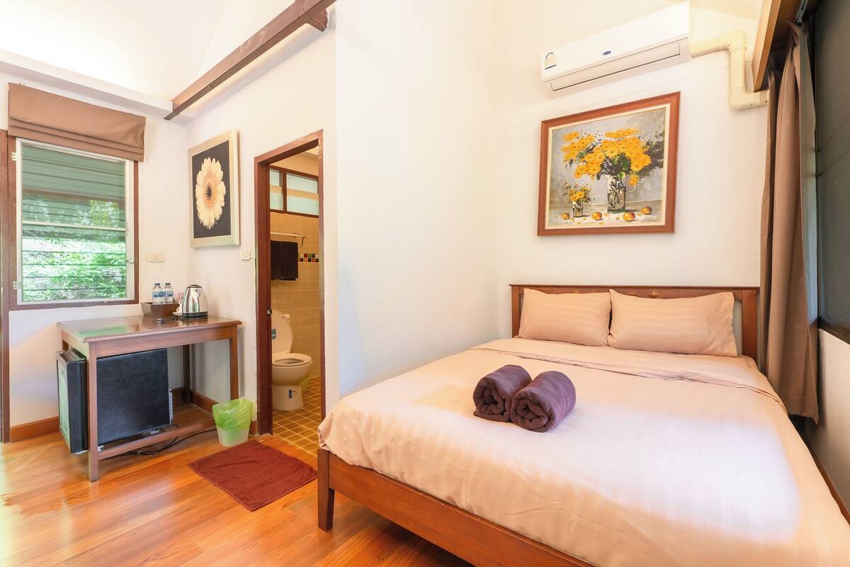 Une chambre d’hôtel avec un lit en bois, un bureau avec un ordinateur, une fenêtre avec des stores et un tableau accroché au mur.