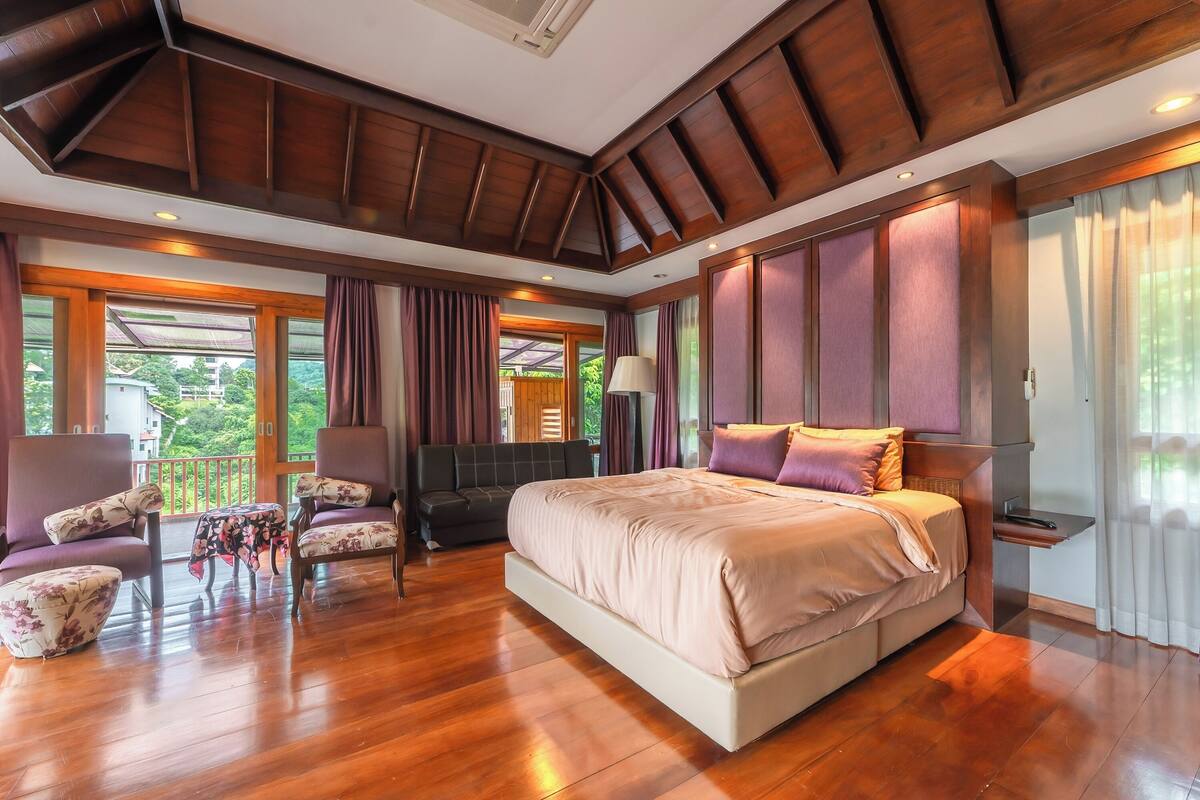 Une chambre spacieuse avec un grand lit, un plancher en bois et un balcon agrémenté de rideaux.
