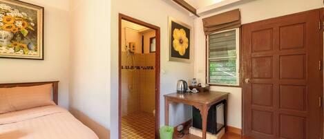 A bedroom with a bed, a wooden table, a door, and a shower area.