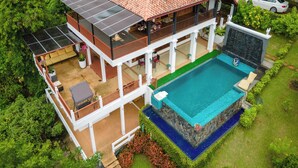 Una casa a due piani con piscina, pannelli solari e un'auto parcheggiata nelle vicinanze.
