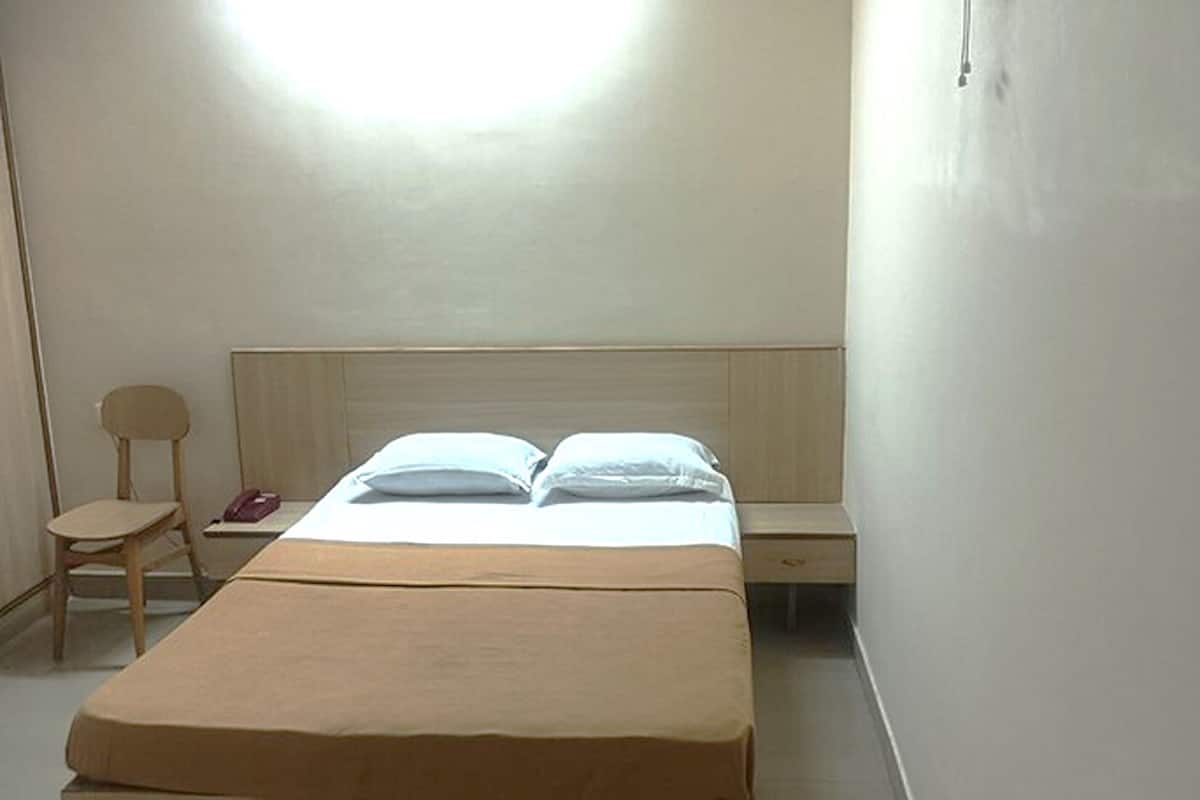 A single bed with a wooden headboard, a bedside table, and a chair in a simple, well-lit room.