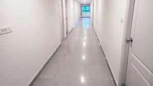 En lång, smal hall med vita väggar och ett glänsande, kaklat golv.