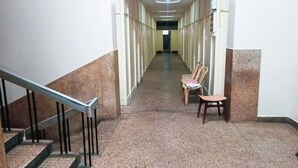 En lång, smal korridor med ett heltäckningsmatta på golvet, ett ledstång på vänster sida och en stol på höger sida.