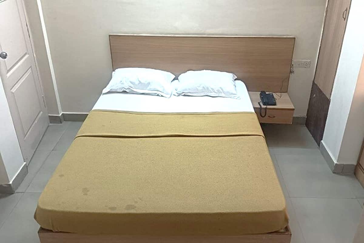 A single bed with a wooden headboard, a bedside table with a phone, and a small cabinet to the right.