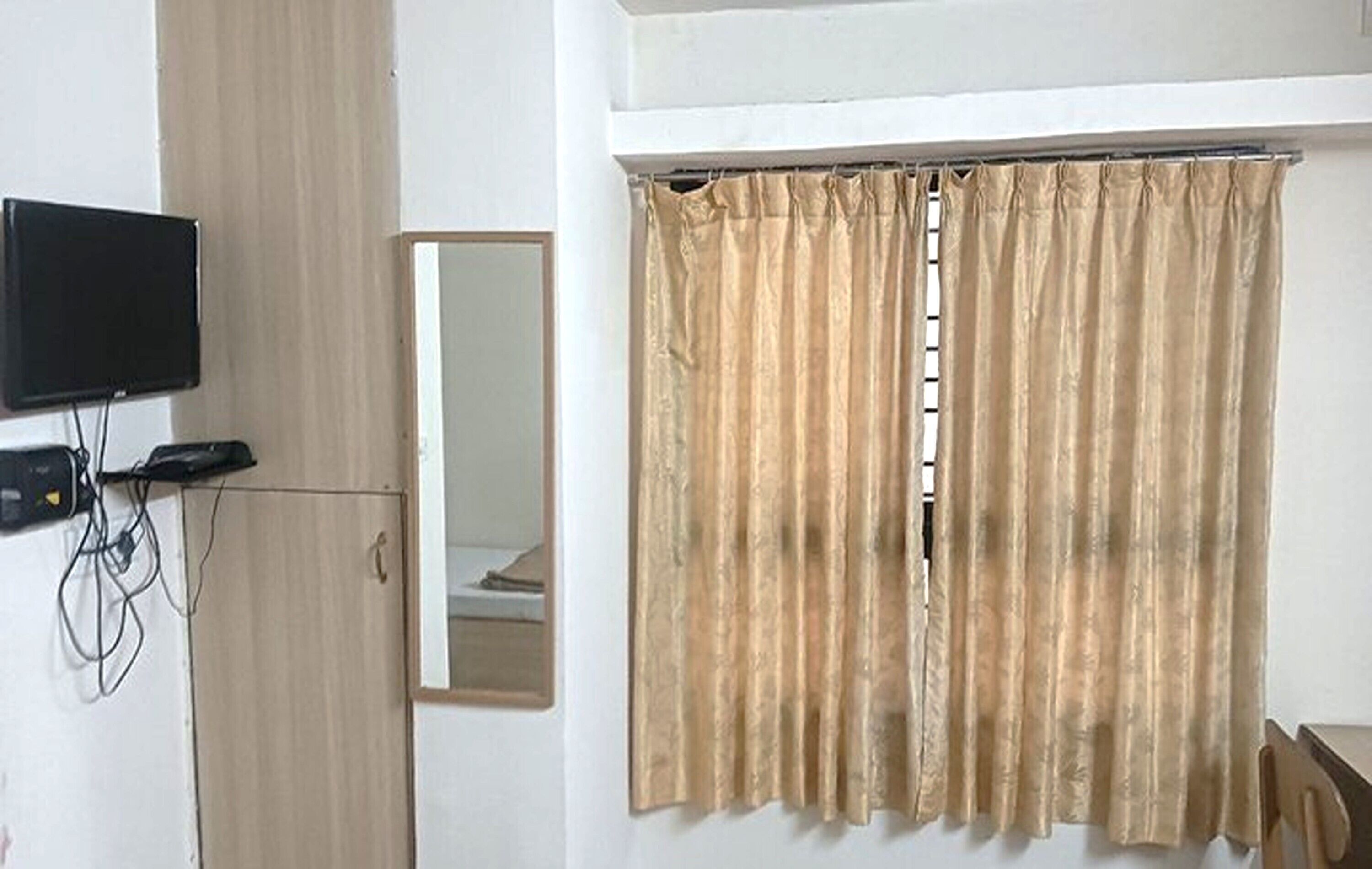 Una habitación con un televisor en la pared, un espejo y cortinas color beige.