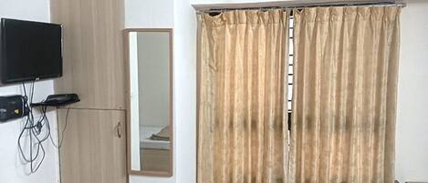 Una habitación con un televisor en la pared, un espejo y cortinas color beige.