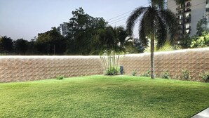 A well-maintained grassy area with a brick wall and a palm tree. - Swastika Homes Near Wave City Center Noida (Noida)