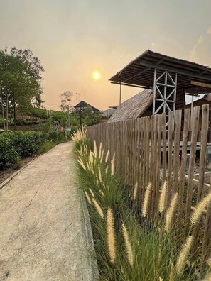 A pathway lined with tall grasses and a wooden fence, leading to a building with a sloped roof and a metal framework. - Fuang Dao Mountain Resort (Muang Fuang)