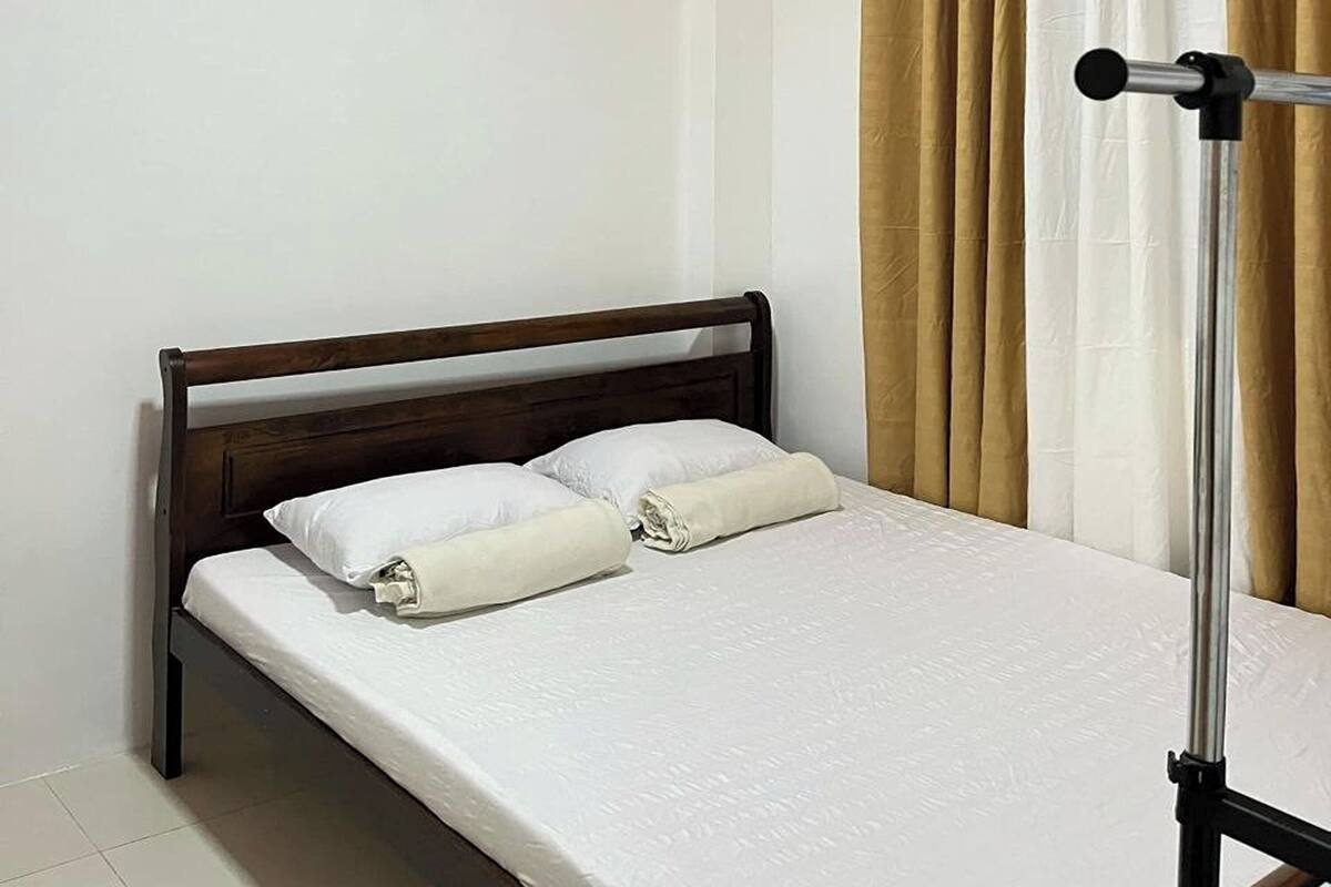 Un lit simple avec une tête de lit en bois, du linge de lit blanc et un pied de lit en métal.