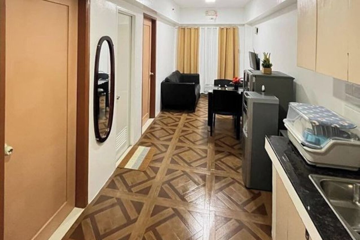 Quarto de hotel compacto com piso estampado, uma pequena cozinha compacta, área de refeições com mesa e cadeiras, e um sofá.