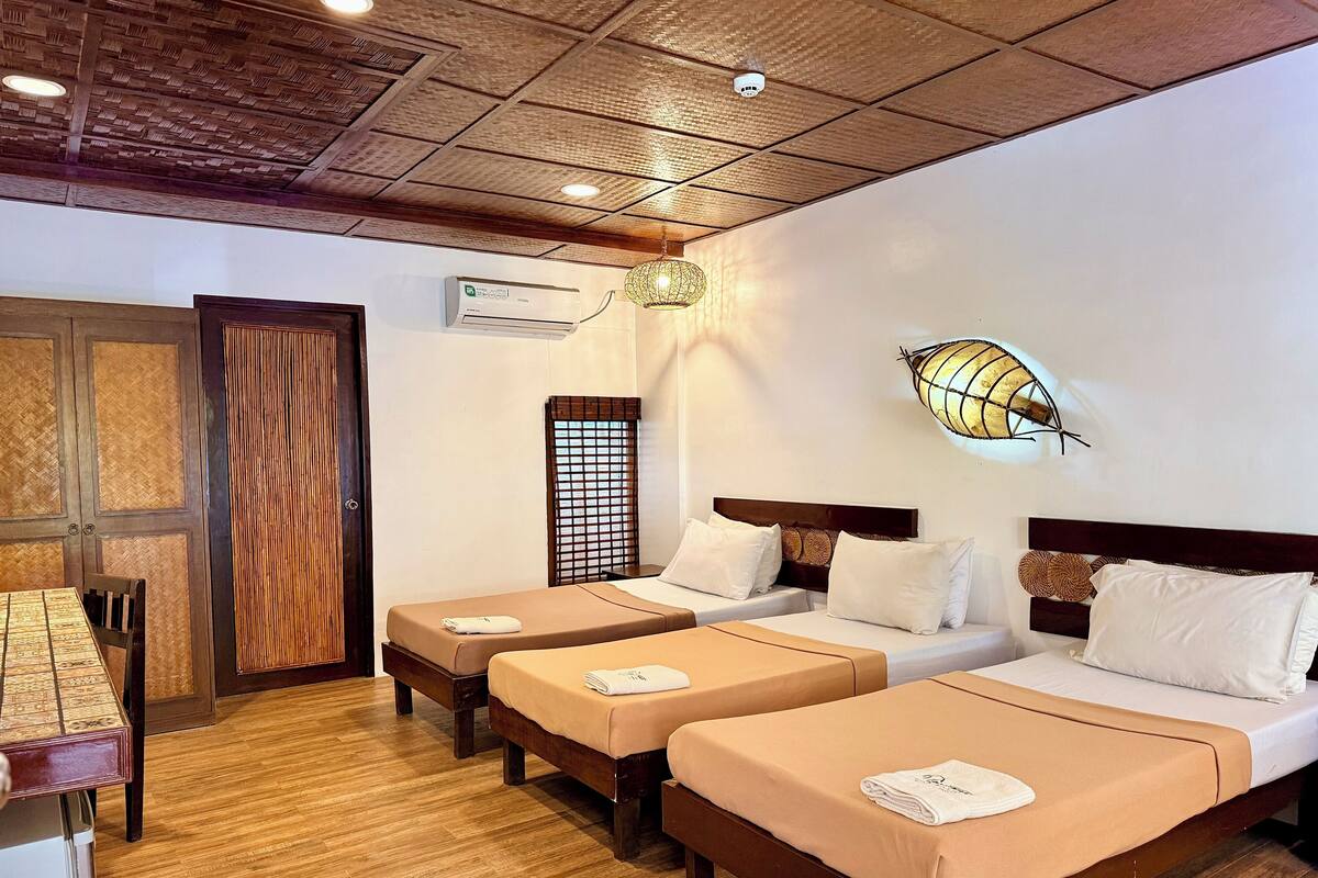 Une chambre d’hôtel avec trois lits, un plafond en bois, un appareil de climatisation et une lampe fixée au mur.