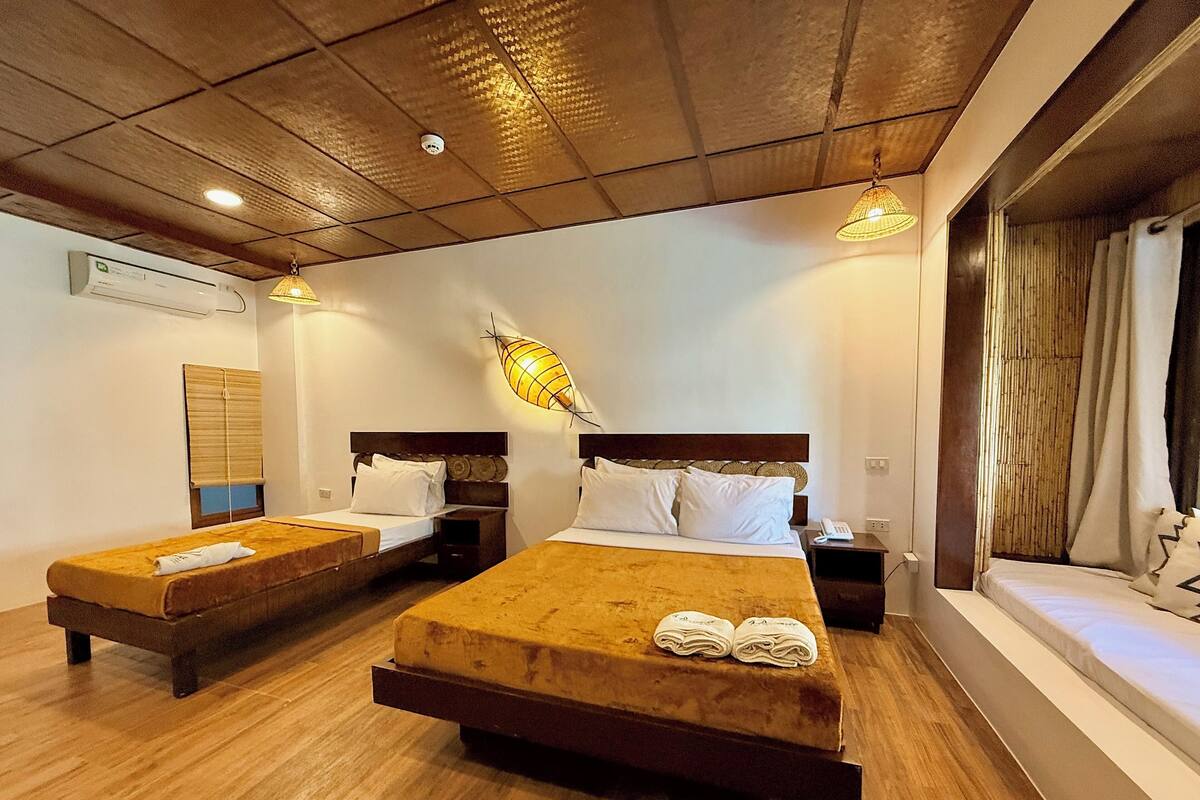 Une chambre d’hôtel avec deux lits, un plancher en bois, un climatiseur fixé au mur, un luminaire au plafond et un téléphone sur la table de chevet.