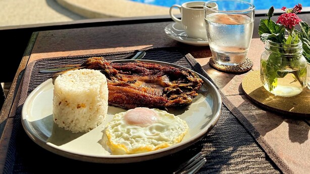 Una mesa con un plato de pescado frito y arroz, una taza de café y un vaso de agua.