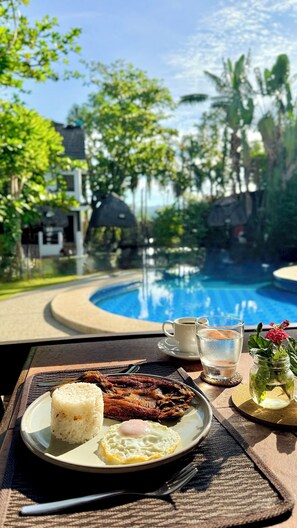 A dining table with a plate of fried fish and rice, a cup of coffee, and a glass of water. - Maritoni Bali Suites And Villas (Bauang)