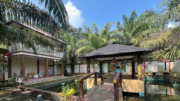 A pool area with a wooden bridge, a gazebo, and a building with a balcony. - Villa Zahira & House 2 (Jambi)
