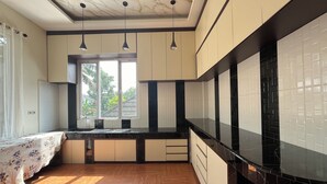 A modern kitchen with wooden flooring, black countertops, and white cabinets. There is a window providing natural light and a view of greenery outside. - Villa Zahira & House 2 (Jambi)