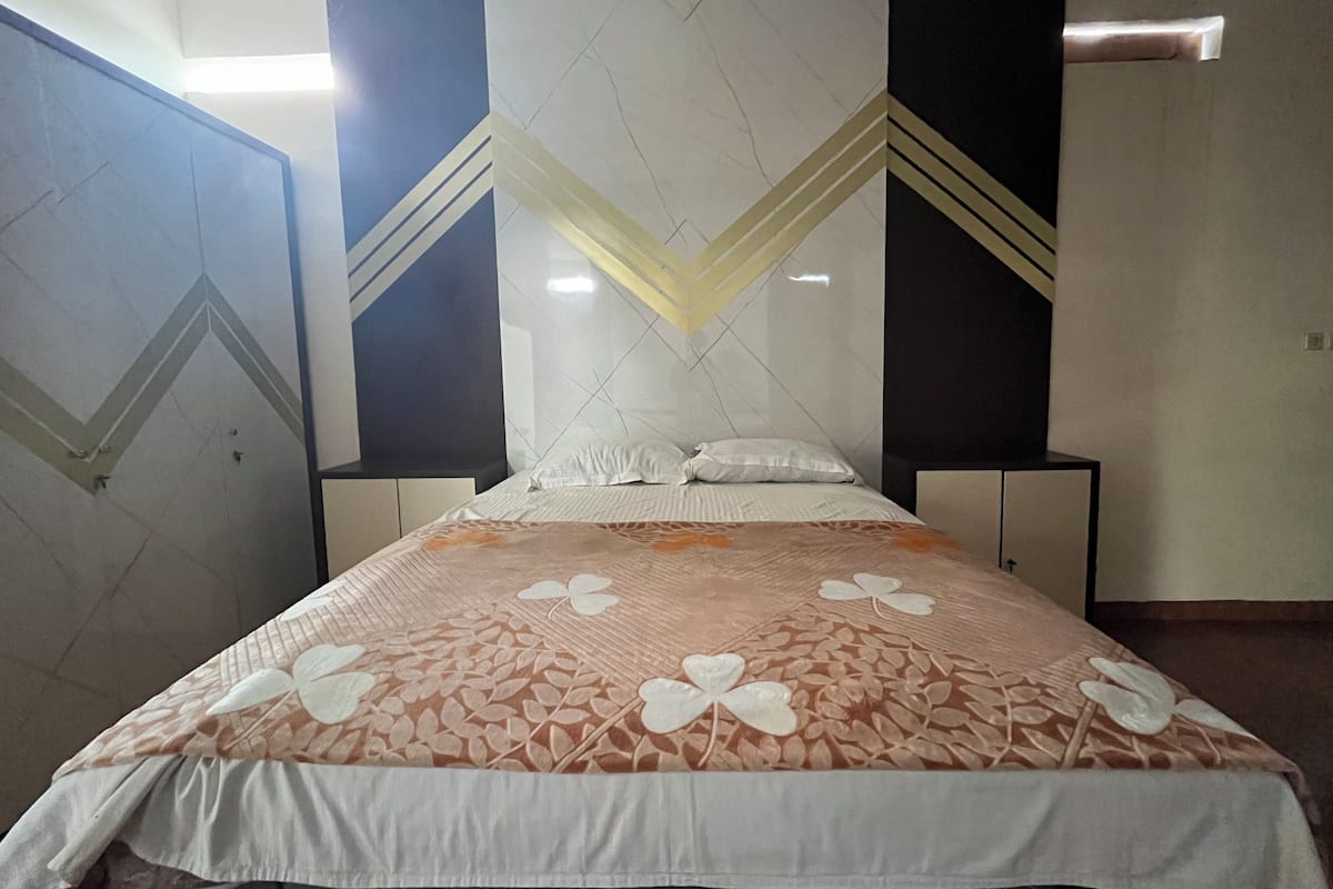 Une chambre d’hôtel comprenant un lit, deux tables de chevet, une tête de lit décorative et un mur orné d’un motif géométrique.