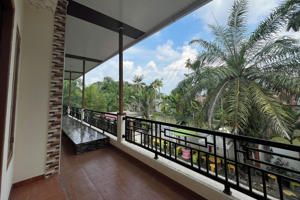 A balcony with a wooden floor, a metal railing, and a view of palm trees and greenery.