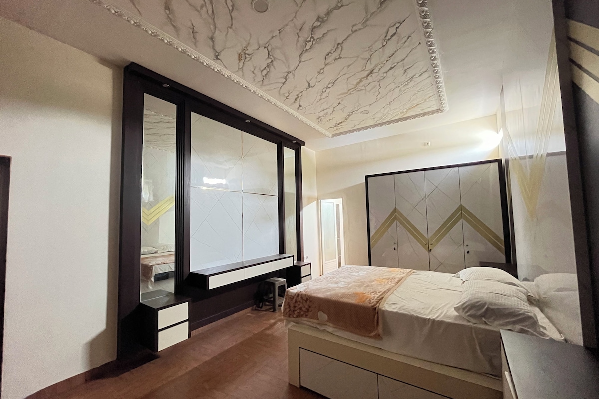 A bedroom with a bed, a wardrobe, a mirror, and a ceiling with a marble design.