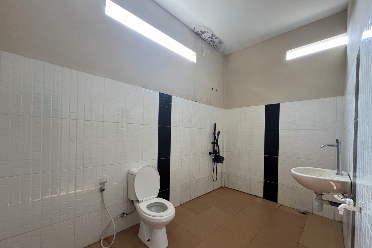 Un baño con paredes de azulejos blancos, un inodoro, ducha y lavabo.