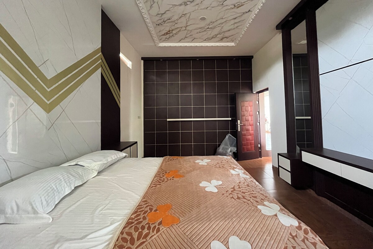A modern bedroom with a marble ceiling, a large bed with a patterned bedspread, a dark tiled wall, and a large mirror.