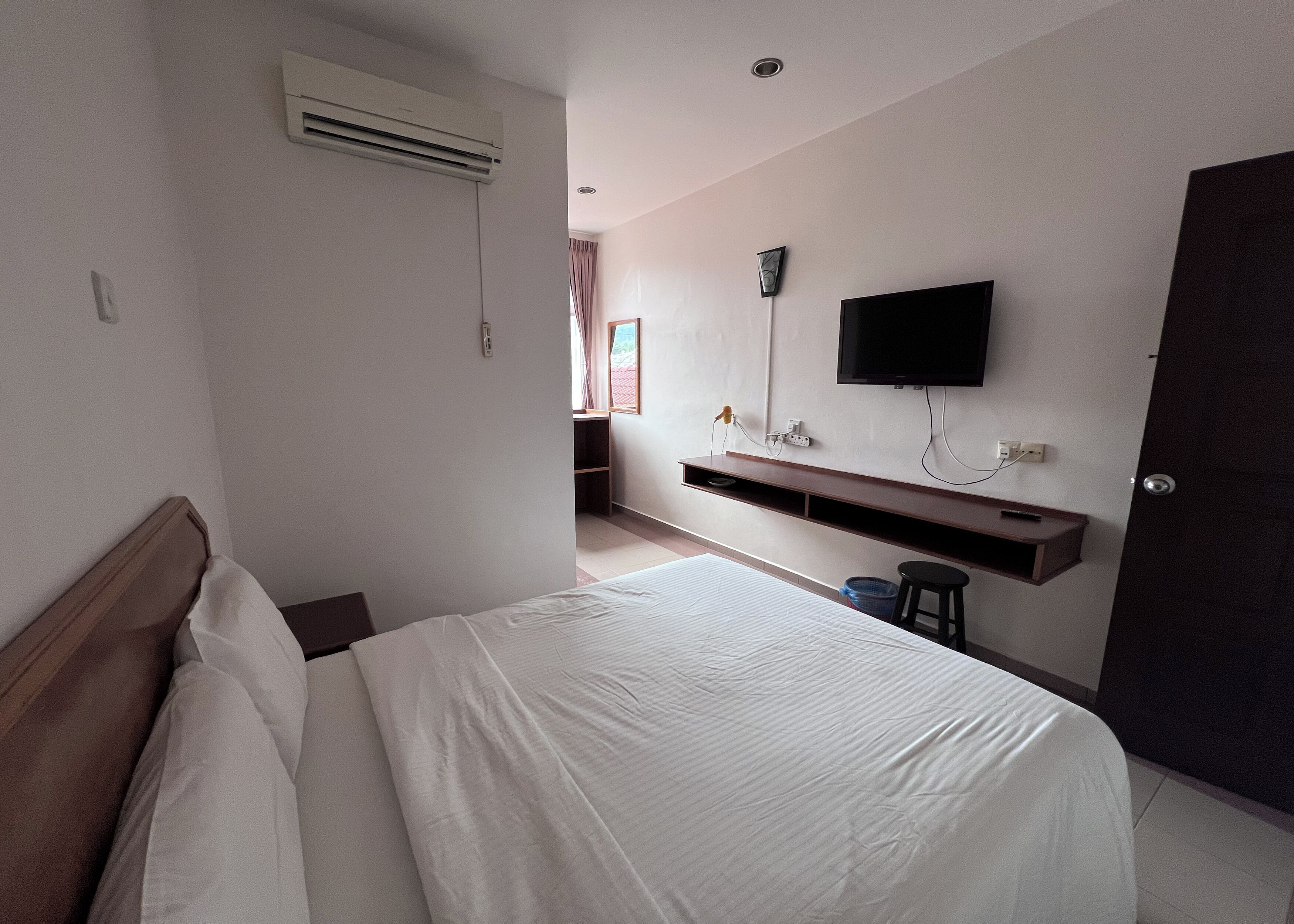 Une chambre d’hôtel avec un lit, un téléviseur fixé au mur, un bureau avec une chaise et une porte.