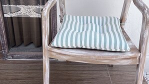 Une chaise en bois rustique, dotée d’un coussin à rayures, est placée sur un sol carrelé.