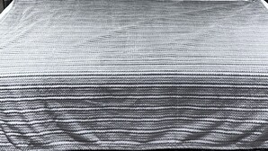 Un lit avec un drap blanc et une couverture à motifs, une tête de lit en bois et une décoration murale en macramé.