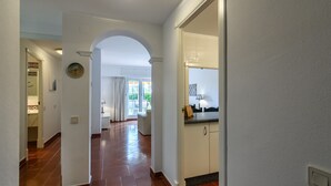 A hallway with a tiled floor, an archway, and a kitchen area with cabinets and a countertop.