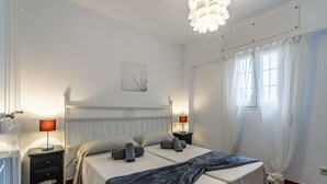 A hotel room with two beds, a nightstand with lamps, a wall-mounted artwork, and a large window with curtains.