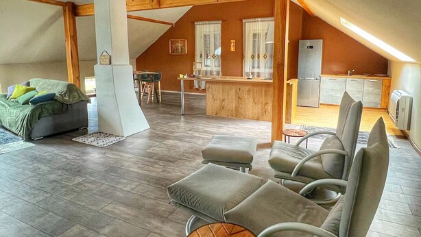 A spacious living area with a sofa set, a small round table, and a kitchen area with a refrigerator and sink. - Spacious loft in the forest (Bining)