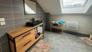 A modern bathroom with a skylight, a wooden vanity, a small table with a chair, and a radiator. - Spacious loft in the forest (Bining)