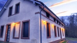 A two-story building with a light-colored facade, multiple windows with shutters, and a visible entrance. - Spacious loft in the forest (Bining)