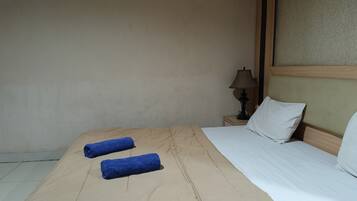 A neatly made bed with a beige bedspread and two rolled blue towels.