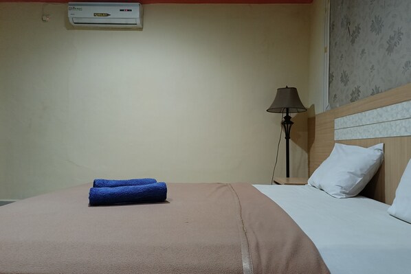 Habitación de hotel con cama, lámpara y aire acondicionado en la pared.