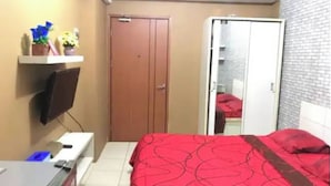 Un dormitorio con una cama, un televisor montado en la pared, un armario y una pequeña estantería con objetos decorativos.