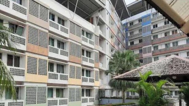 Un edificio residencial de varios pisos con balcones, un espacio al aire libre cubierto con plantas y una estructura con techo de paja.
