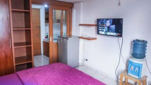 Un dormitorio con cama, televisor montado en la pared, dispensador de agua y un armario de madera.