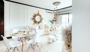 A modern living room with a dining area, white furniture, and a decorative sunburst mirror. - Bali Dream-Luxury Apartment- Power Backup

 (Sandton)