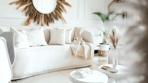 En moderne stue med en hvid sofa, et rundt spejl og et lille rundt bord med en vase og pampasgræs.